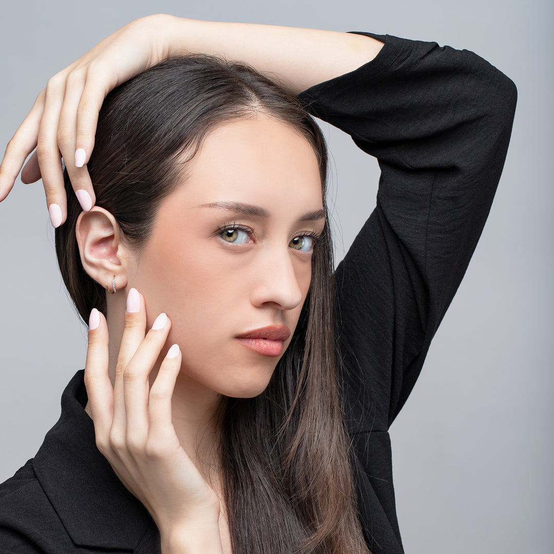 Woman with one hand on her head and the other touching her face against a gray background