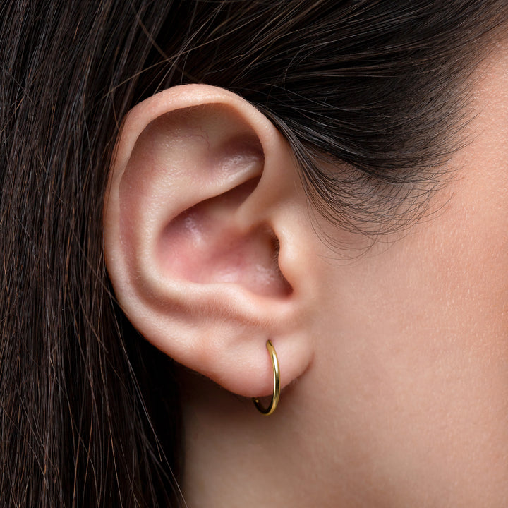 Close-up of an ear wearing a gold hoop earring with dark hair.