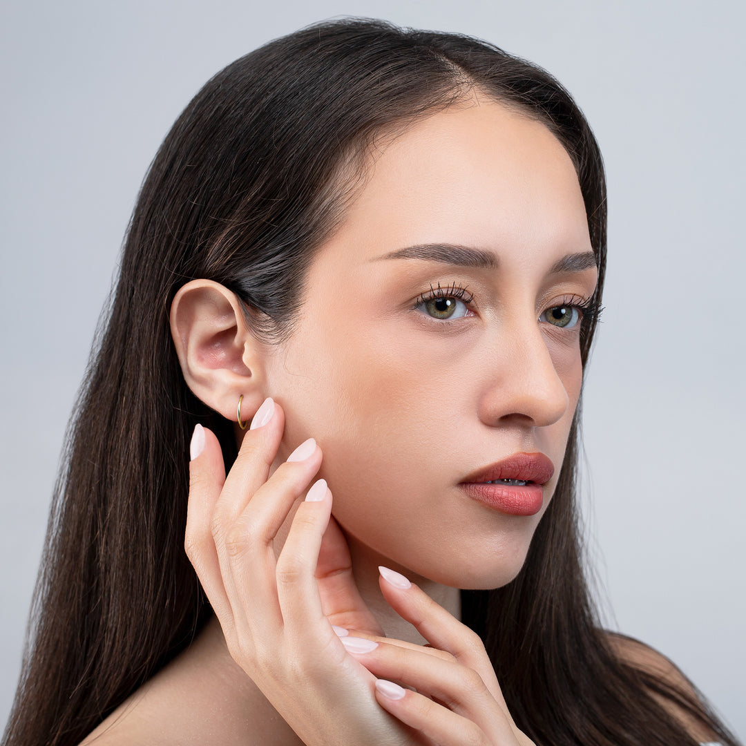 Woman with long dark hair touching her face against a gray background