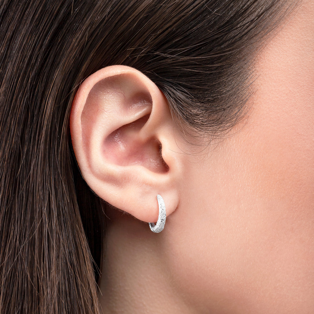 Close-up of an ear wearing a silver hoop earring with dark hair.