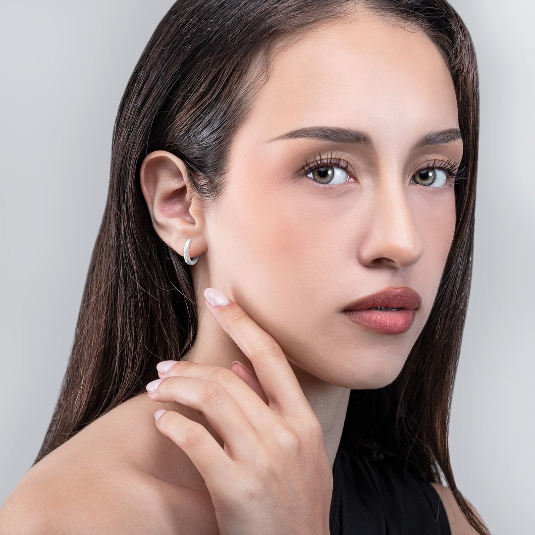 Woman with long dark hair and a neutral expression, wearing a black top against a gray background