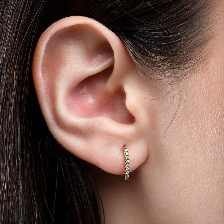 Close-up of an ear wearing a gold hoop earring with a neutral background