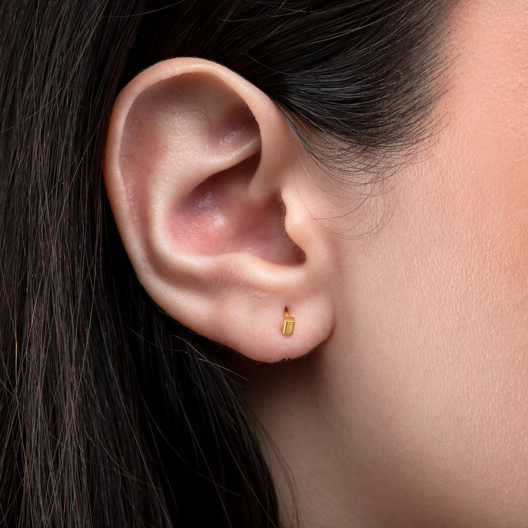Close-up of an ear wearing a gold earring with a blurred background