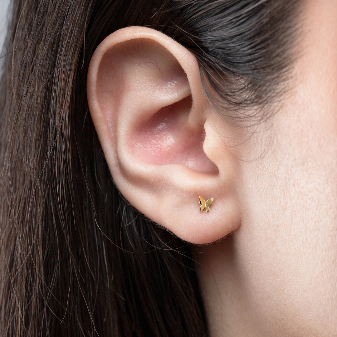 Close-up of an ear wearing a gold earring with dark hair and skin.