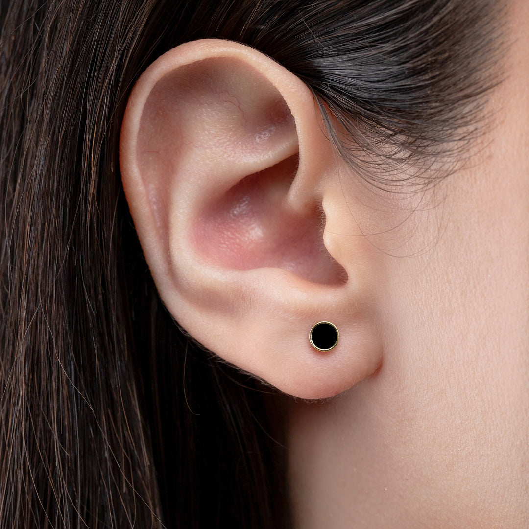 Close-up of an ear wearing a black stud earring with dark hair.