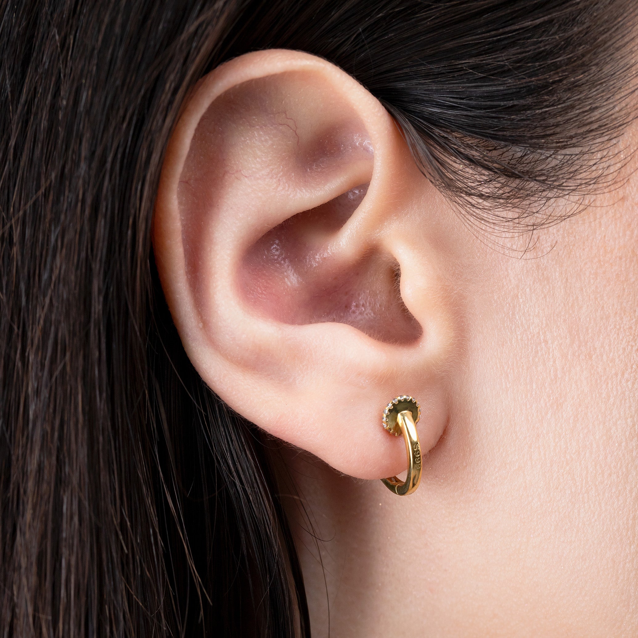 Close-up of an ear wearing a gold hoop earring with dark hair.
