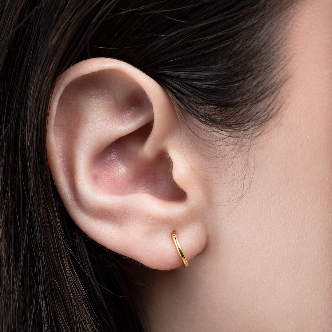 Close-up of an ear wearing a gold hoop earring with dark hair.