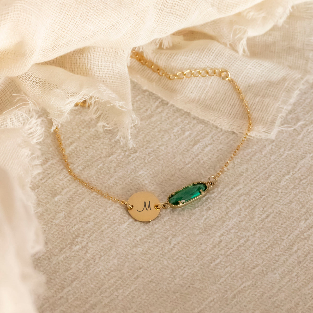 Bracelet with engraved M initial disc and green rectangular stone on beige fabric