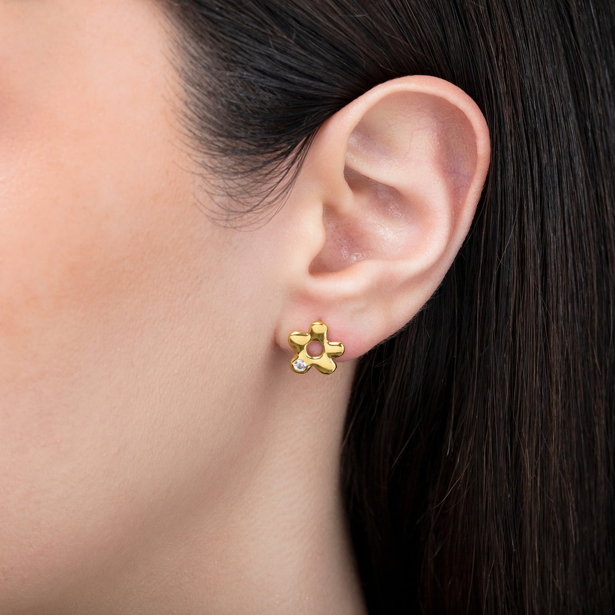 Gold-tone flower stud earring with a clear stone accent worn on the ear in a close-up view
