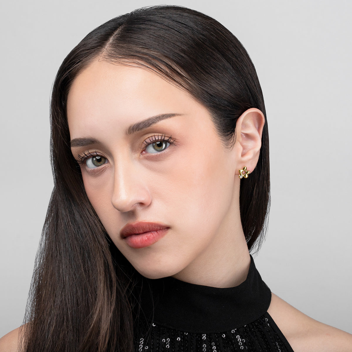 Gold-tone flower stud earring with a clear stone accent worn on the ear in a front-facing portrait