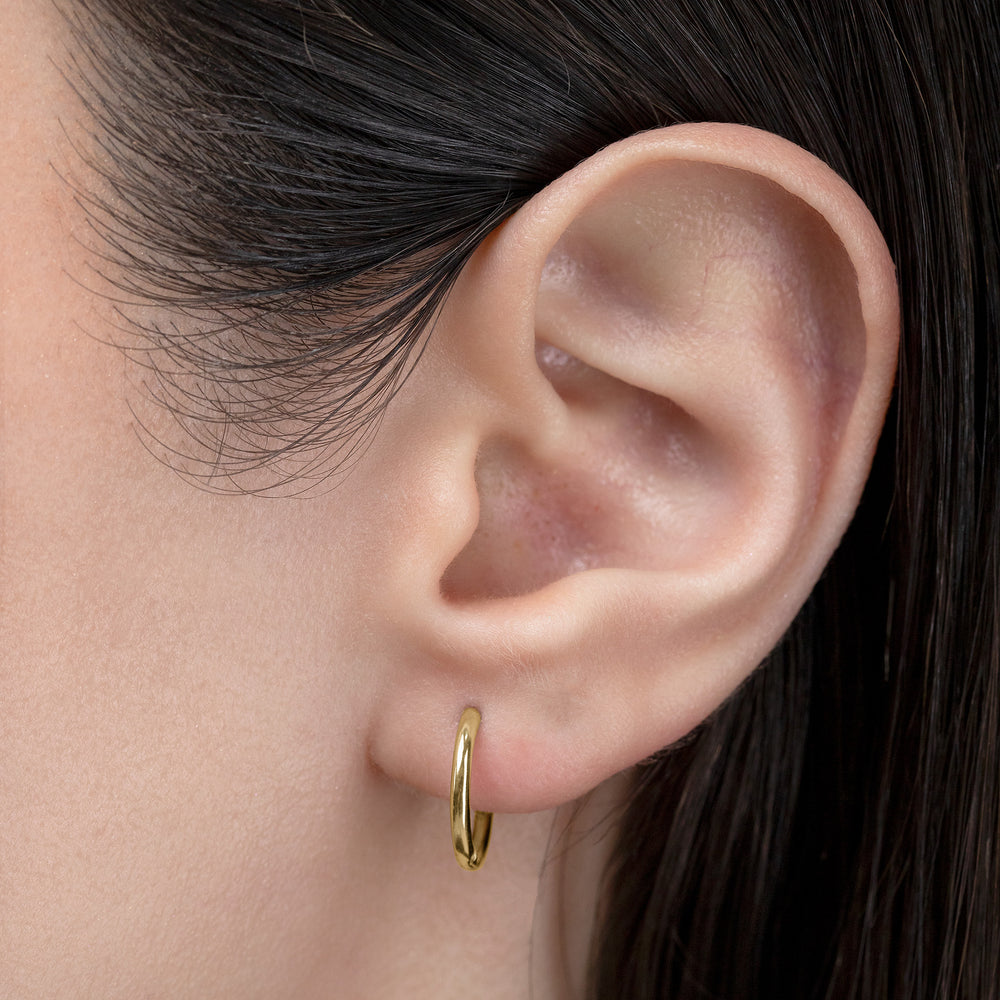 Close-up of an ear wearing a gold hoop earring with dark hair.