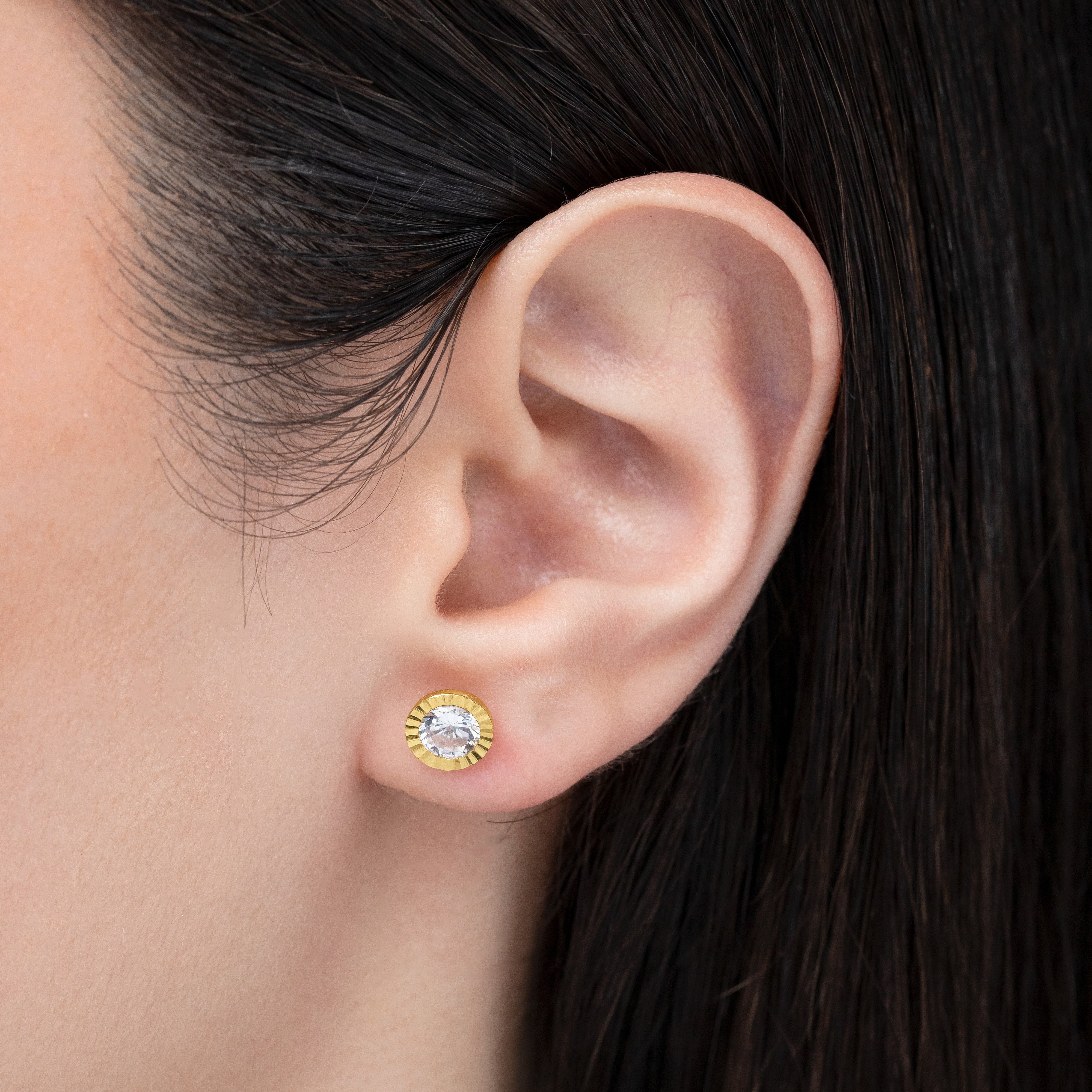 Close-up of an ear wearing a gold and diamond earring with dark hair.