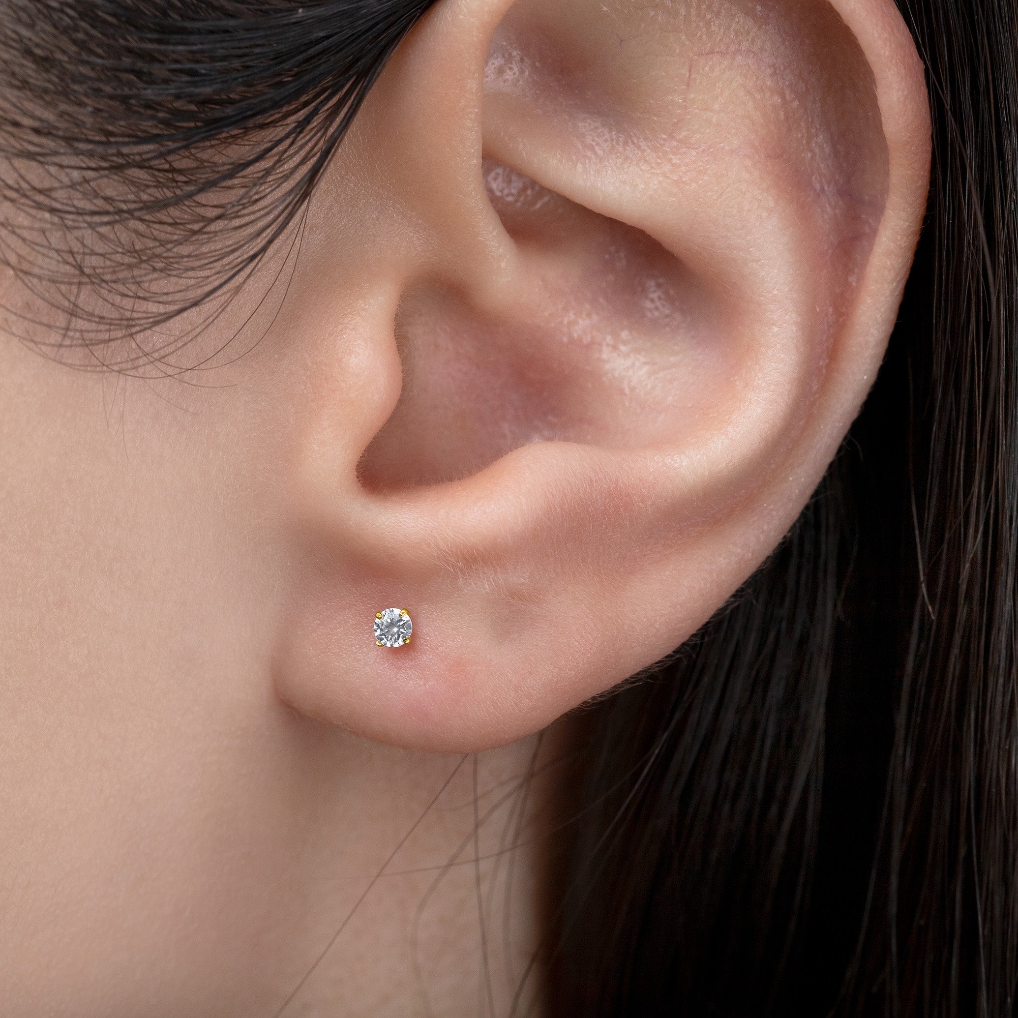 Close-up of an ear wearing a diamond stud earring with dark hair.