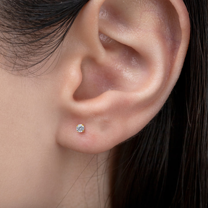 Close-up of an ear wearing a diamond stud earring with dark hair.