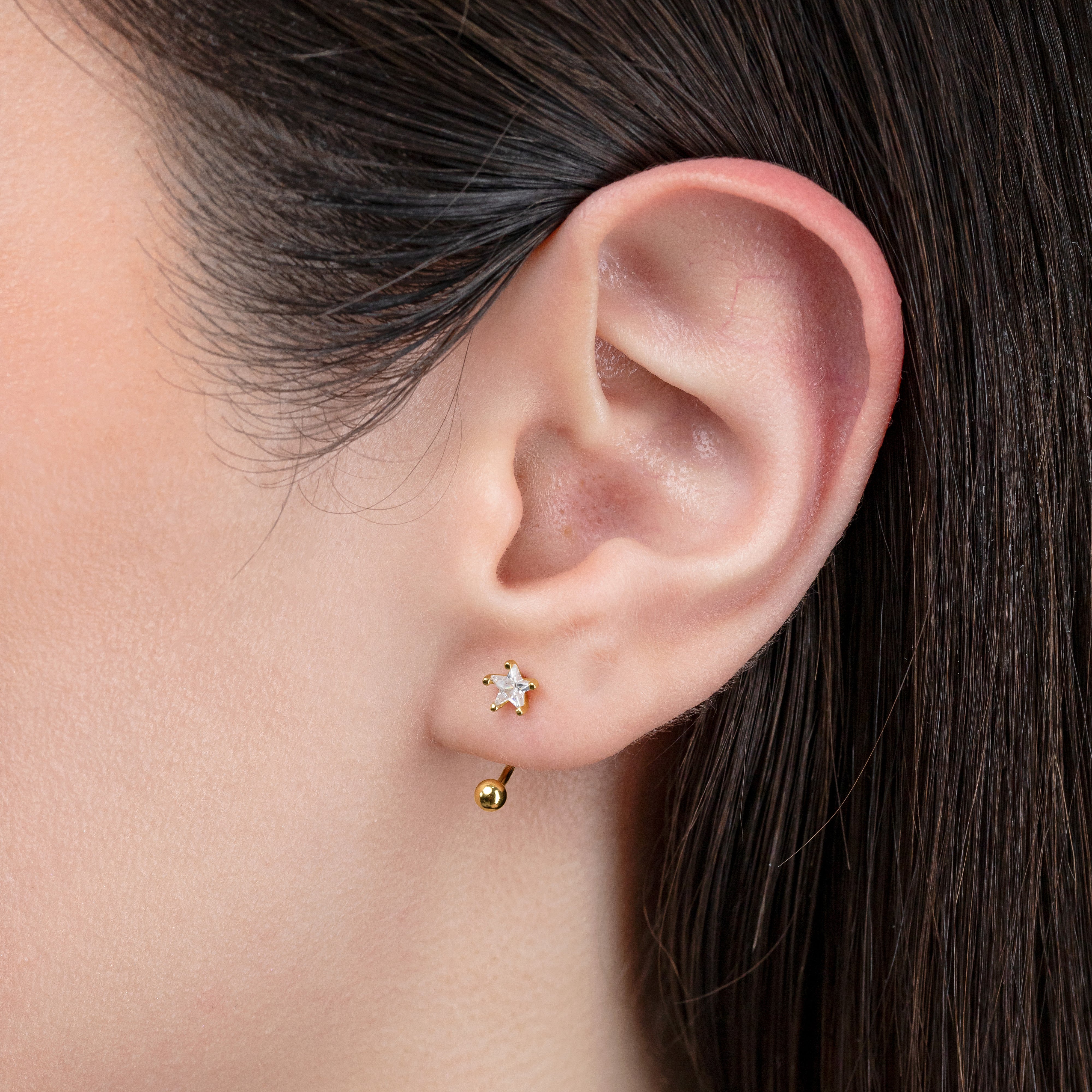 Close-up of an ear wearing a gold earring with a star design.