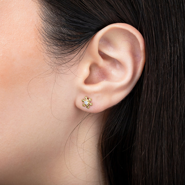 Close-up of an ear wearing a gold earring with a clear gemstone.