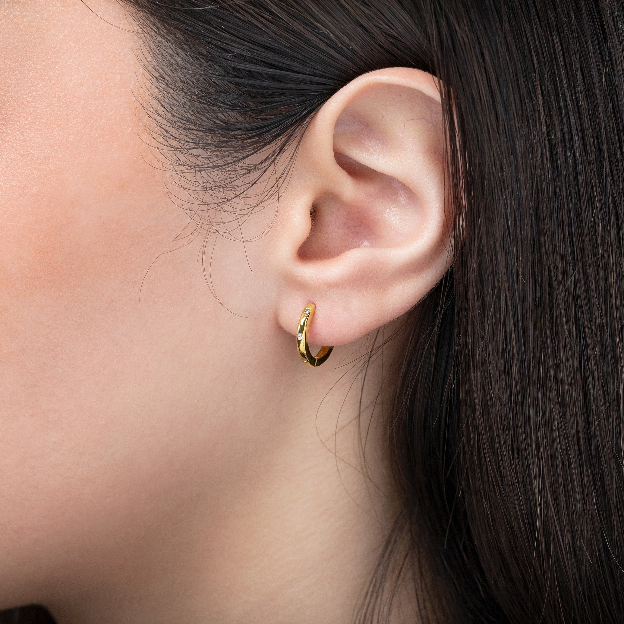 Close-up of an ear wearing a gold hoop earring with dark hair partially visible.