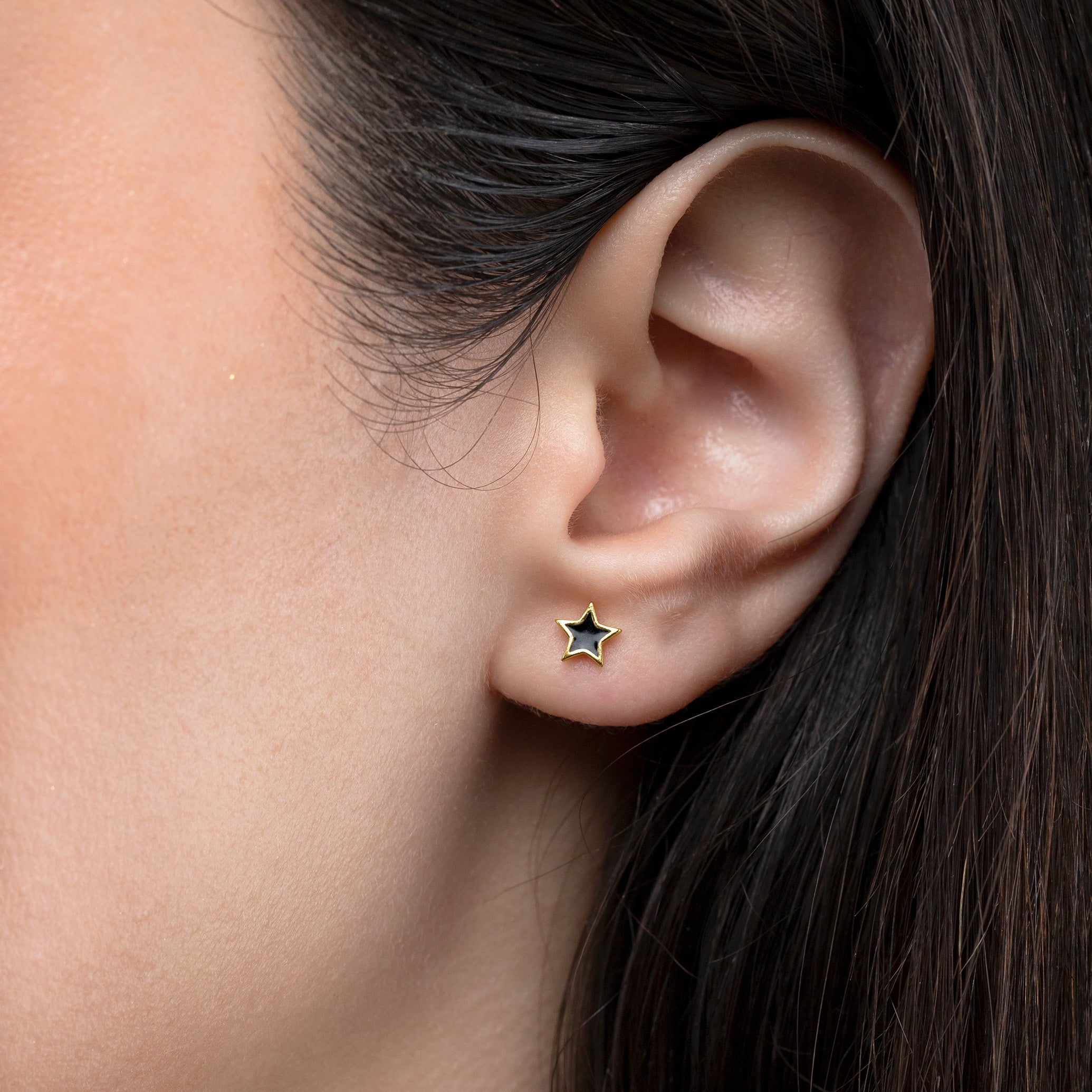 Close-up of an ear wearing a gold star-shaped earring with a black center.