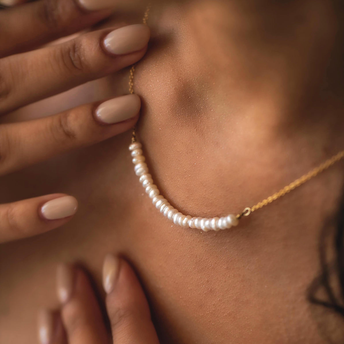 Gold-tone necklace with a centered row of small white pearls worn close to the neckline with a hand nearby