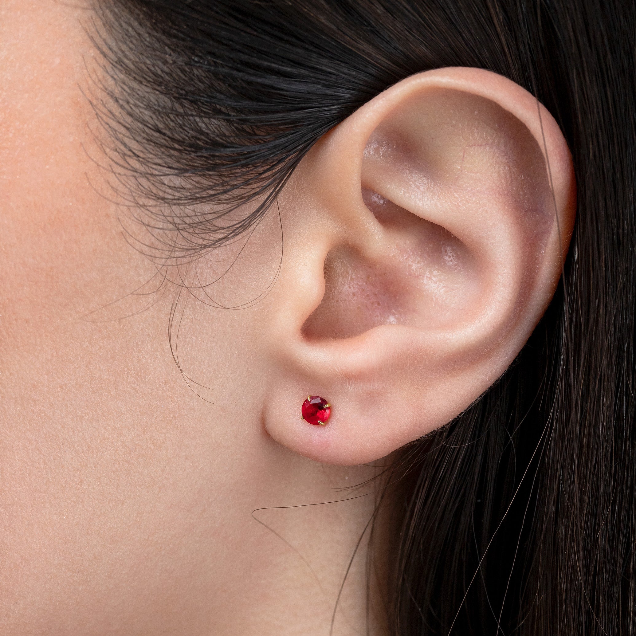Close-up of an ear wearing a red gemstone earring with dark hair.