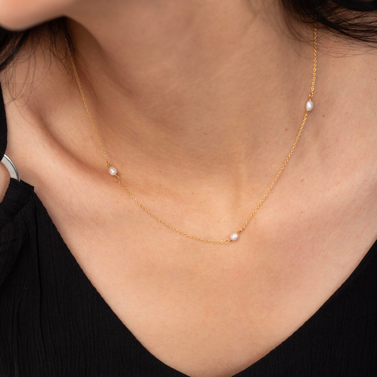 Gold-tone necklace with three small white oval beads worn on a model in a black top