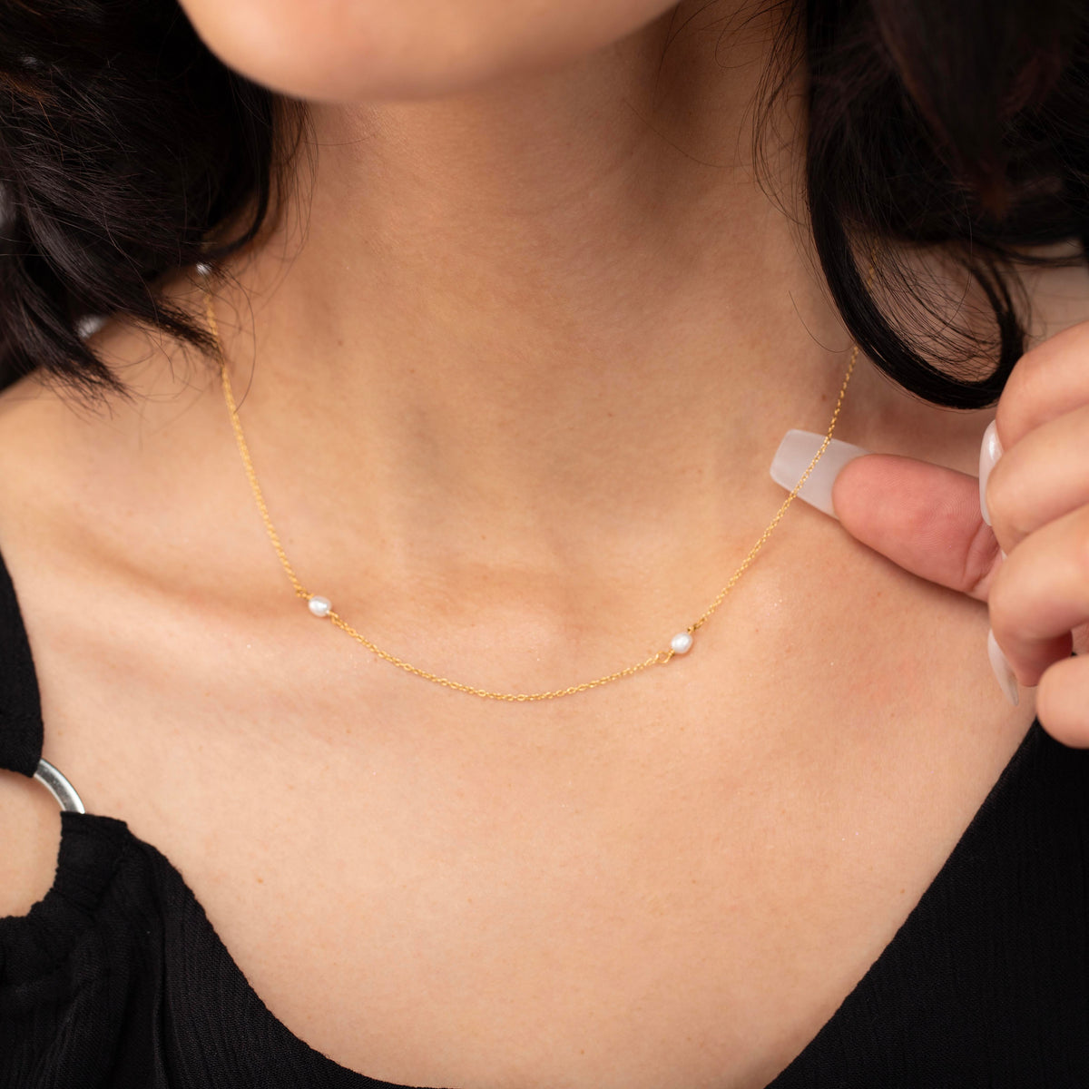 Close-up of a gold-tone necklace with small white oval beads worn on a model adjusting the chain
