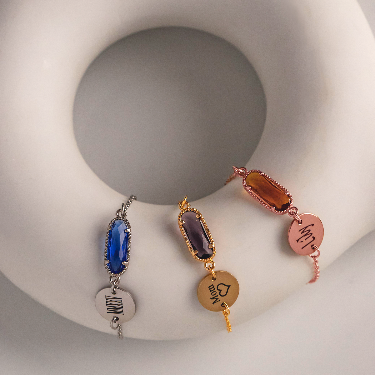 Three bracelets in silver, gold, and rose-gold tones with blue, purple, and amber rectangular stones and engraved round discs