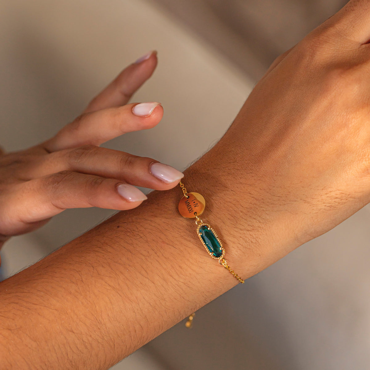 Bracelet with engraved round disc and green rectangular stone worn on a wrist