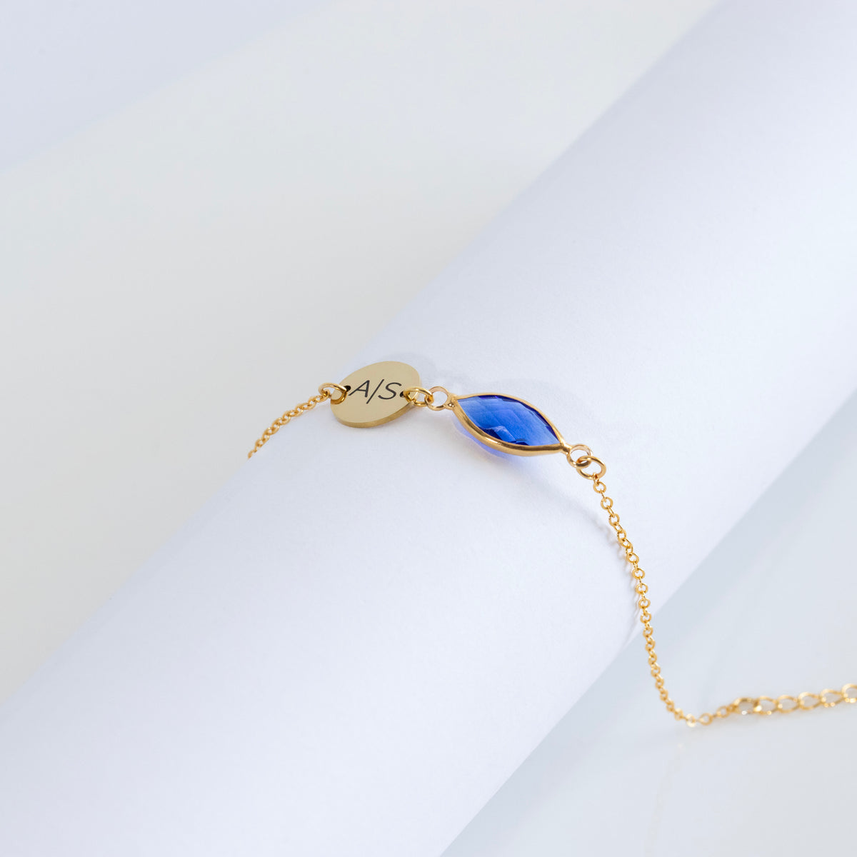 Gold-tone bracelet with engraved round disc and blue faceted marquise-shaped stone on white surface