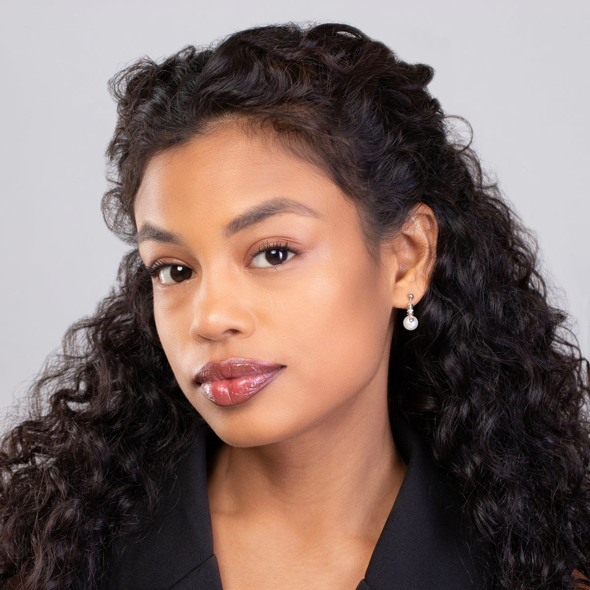Woman with curly hair wearing a black top against a gray background