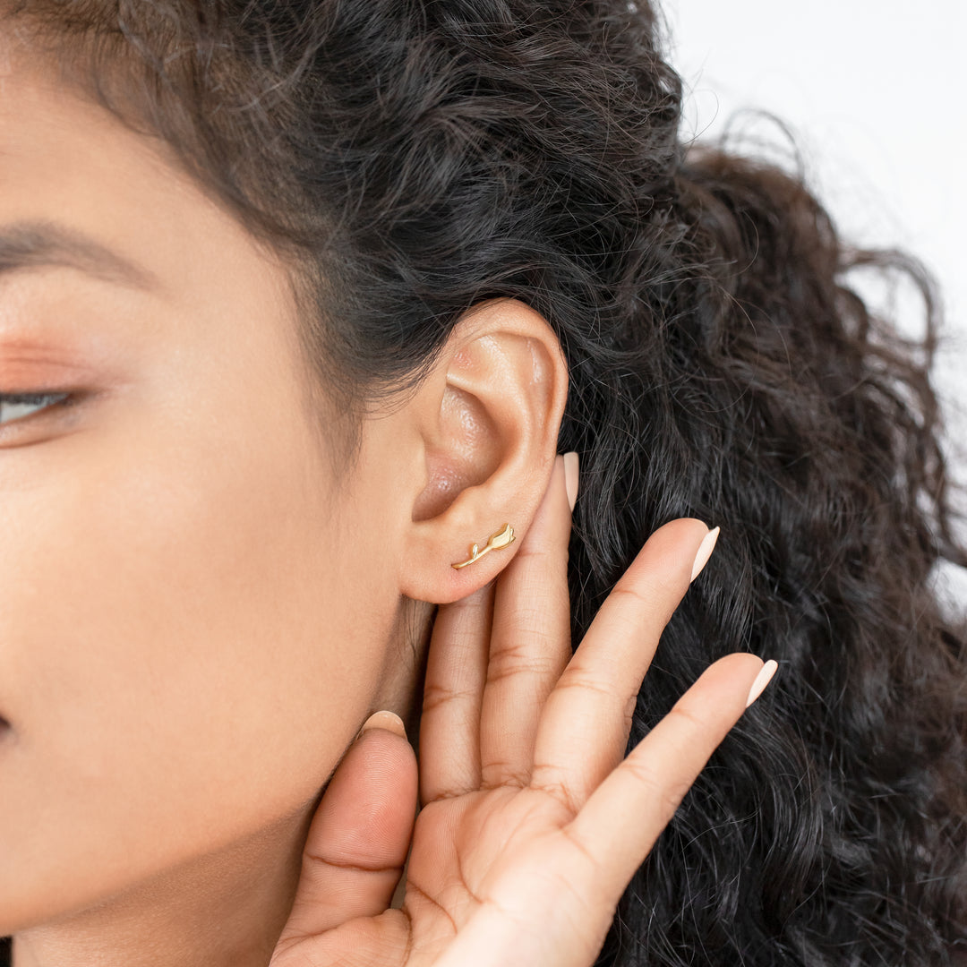 Close-up of a person wearing a gold earring with a neutral background