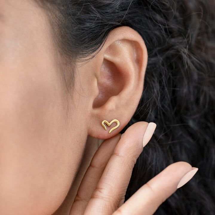 Gold heart-shaped earring worn by a person with dark hair.