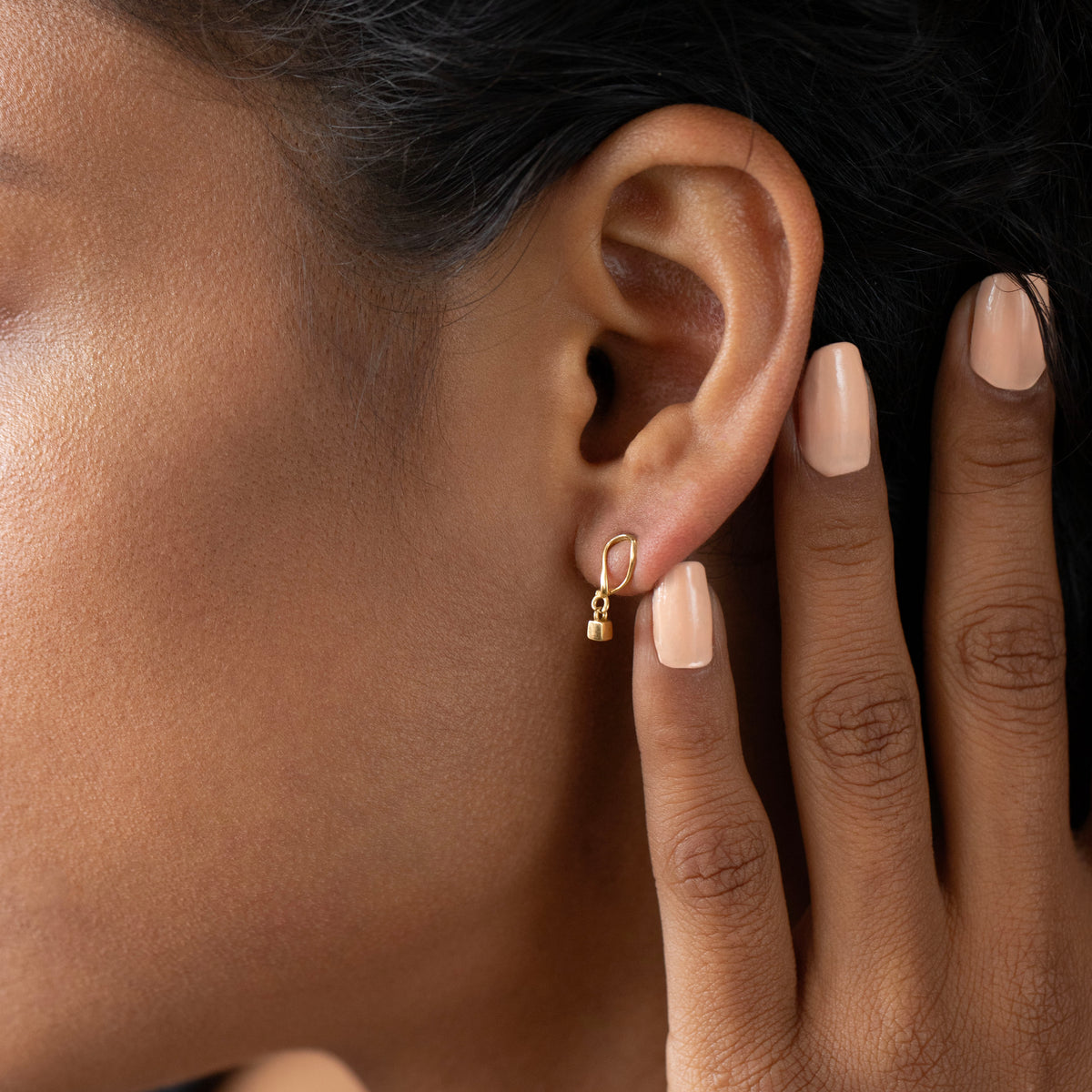 Close-up of an ear wearing a gold hoop earring with a hand touching the earlobe.