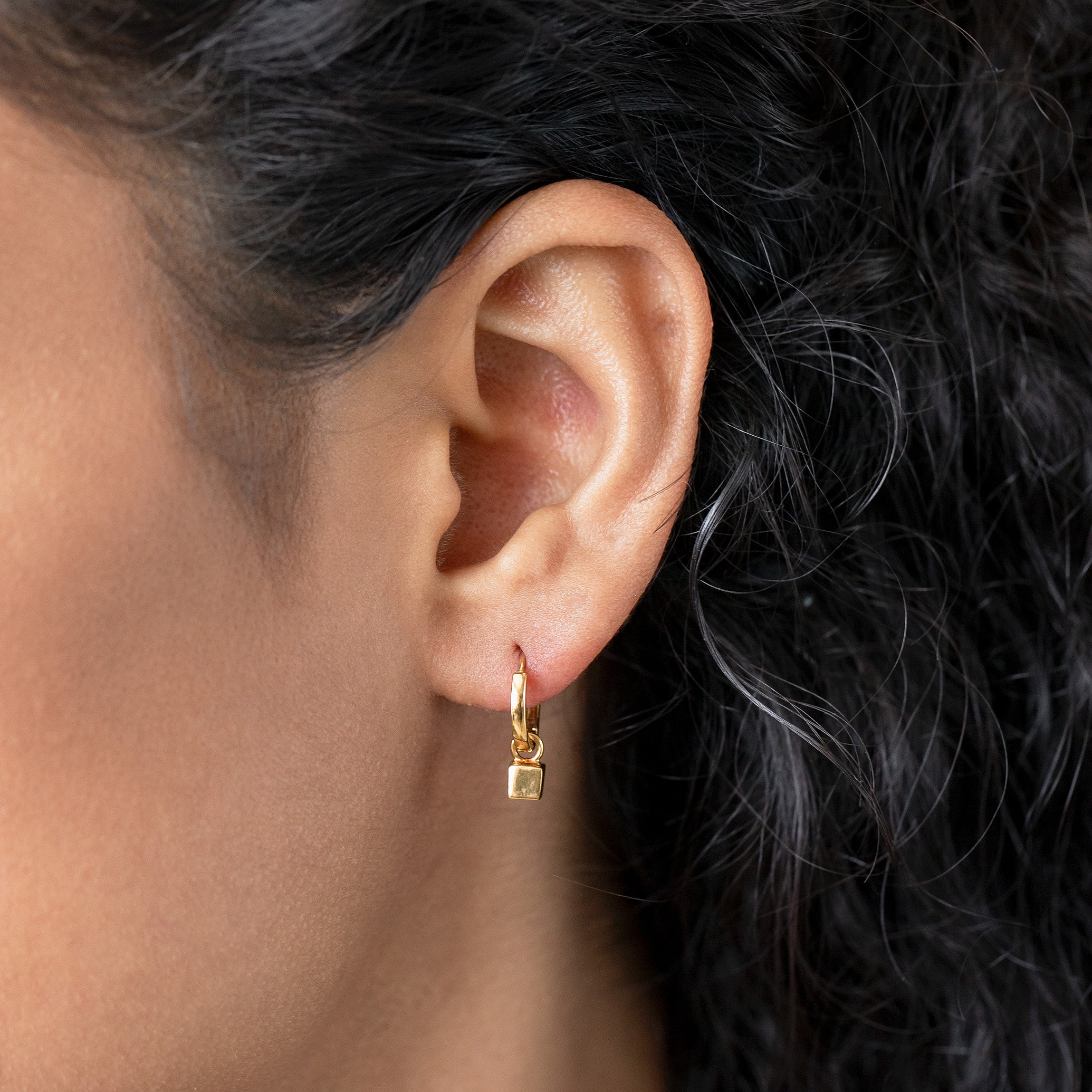 Close-up of an ear wearing a gold earring with dark hair in the background