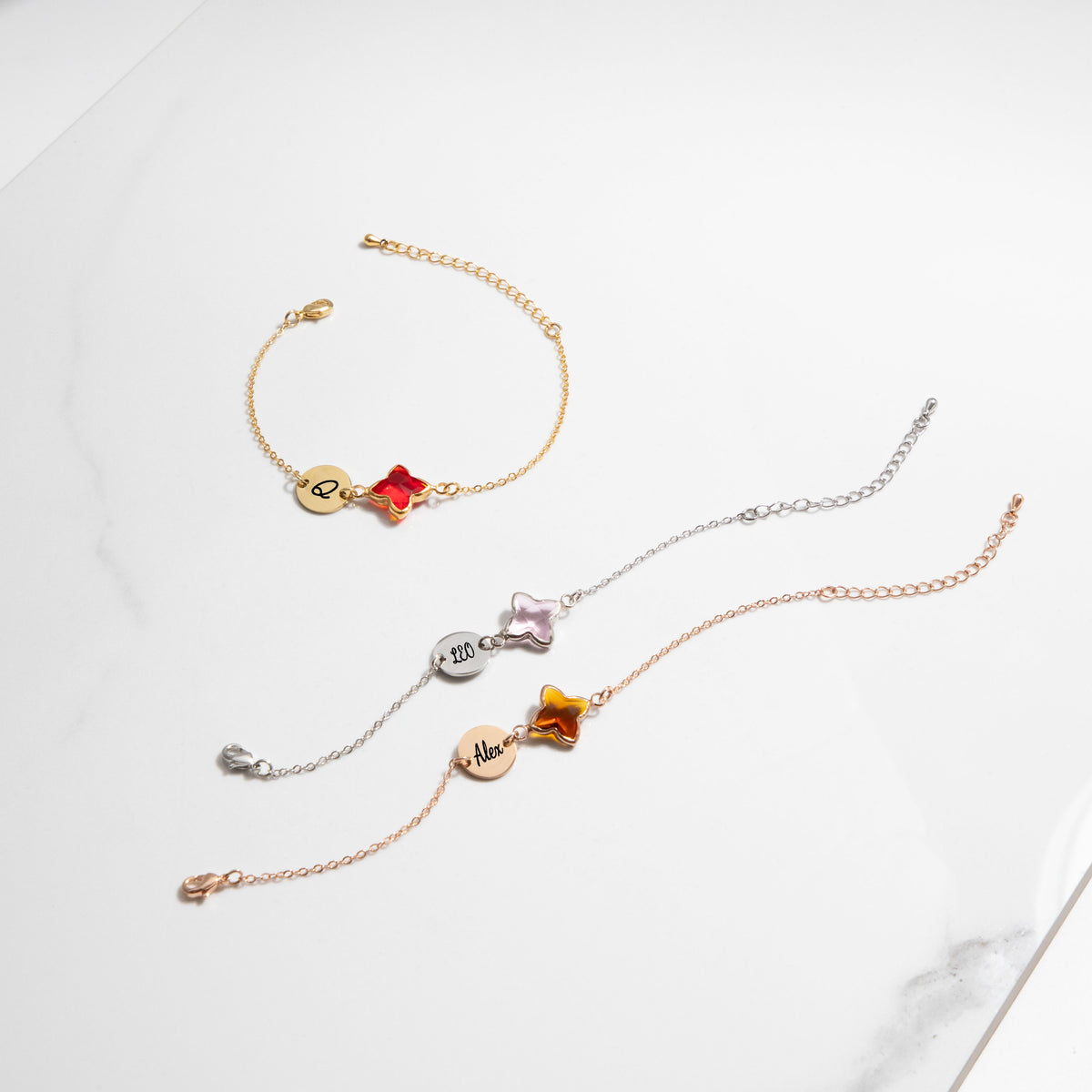 Three bracelets with engraved round discs and red, light pink, and amber four-lobed stones on a white surface