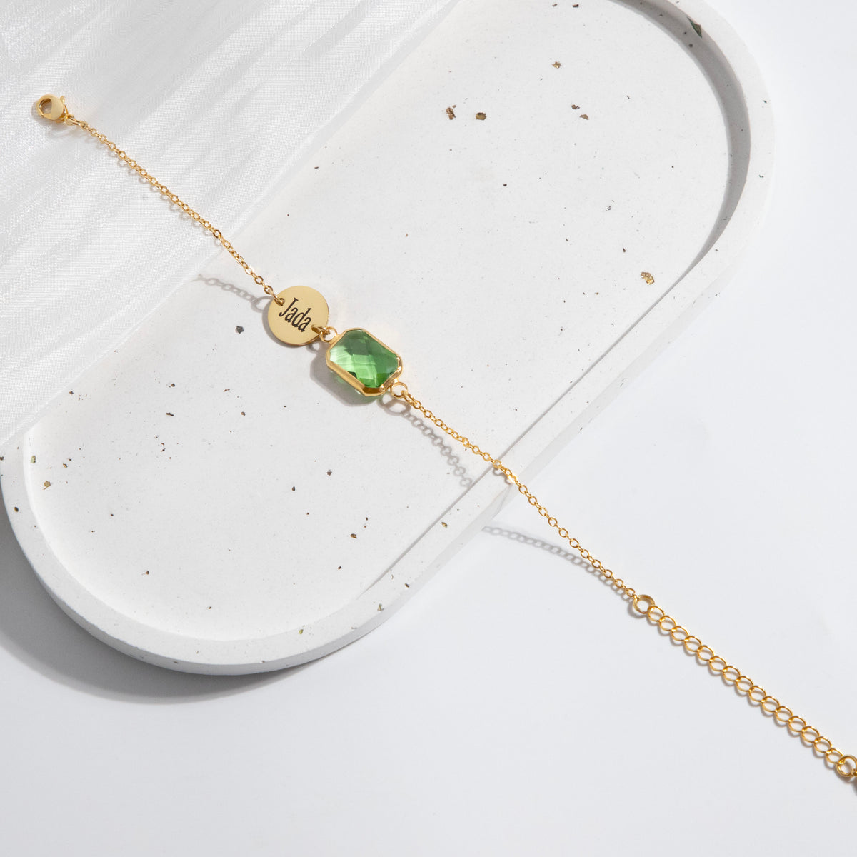 Gold-tone bracelet with engraved round disc and green faceted rectangular stone on a white display surface