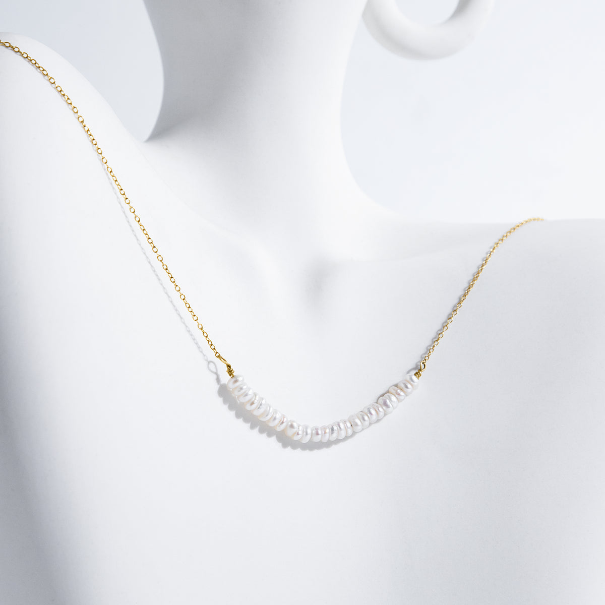 Gold-tone necklace with a centered row of small white pearls displayed on a white sculptural surface