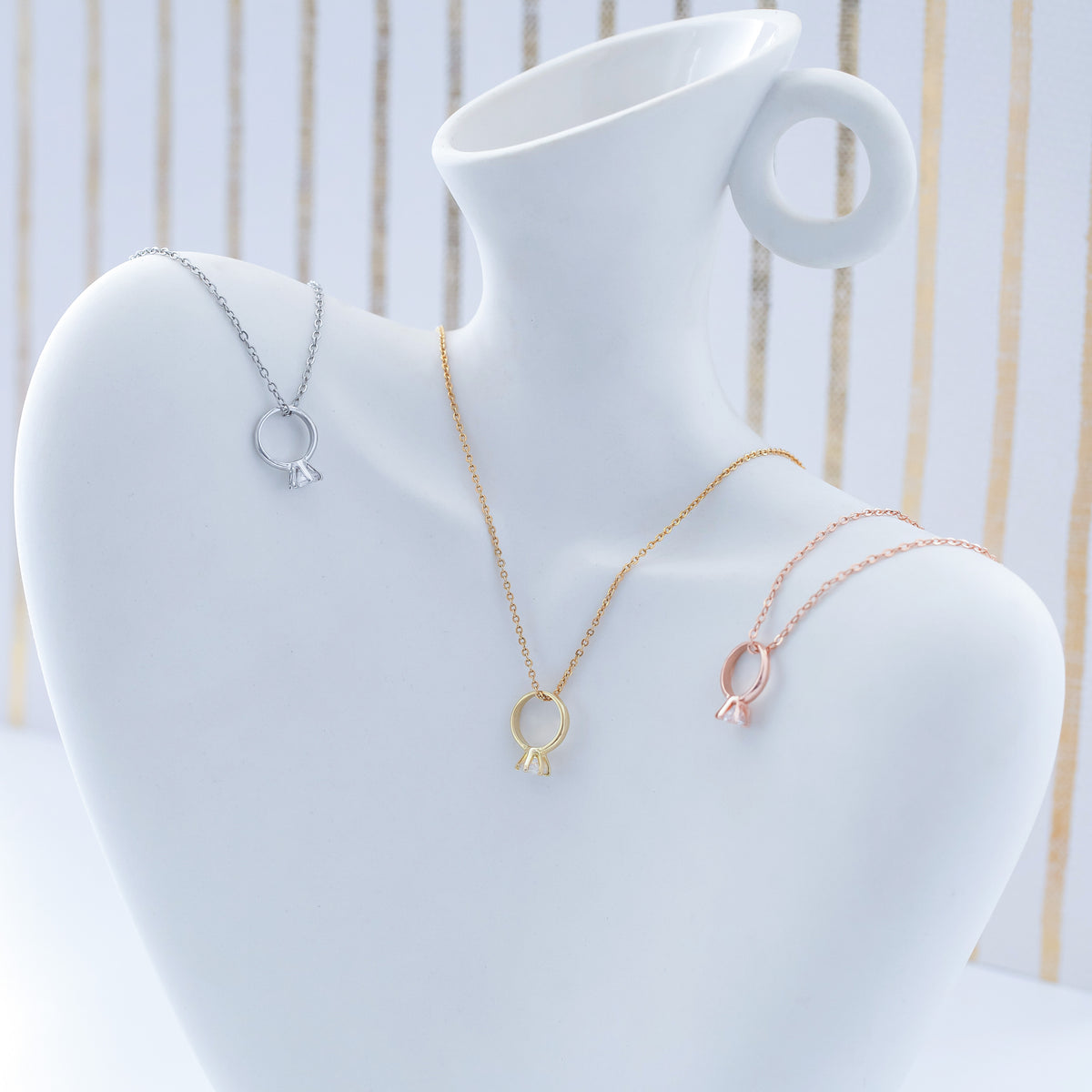 Gold-, silver-, and rose-gold-tone necklaces with ring-shaped charms displayed on a white jewelry bust