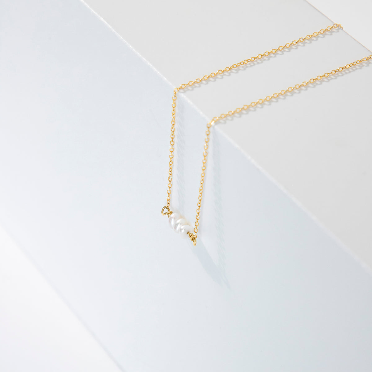 Gold-tone necklace with a short row of white oval pearls displayed on a white geometric surface