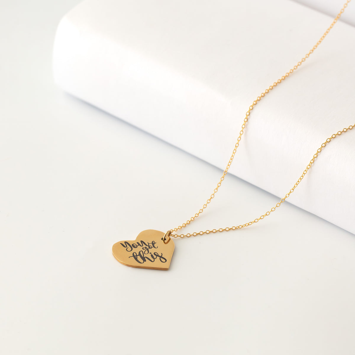 Gold-tone heart pendant necklace with handwritten engraving displayed on a white surface
