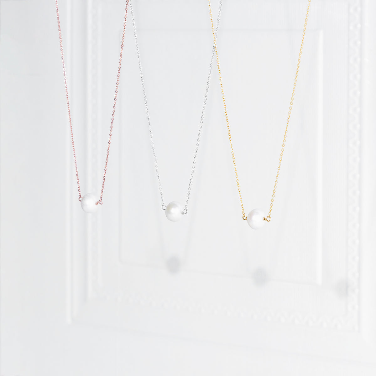 Three delicate necklaces in rose-gold, silver, and gold tones, each with a single white pearl