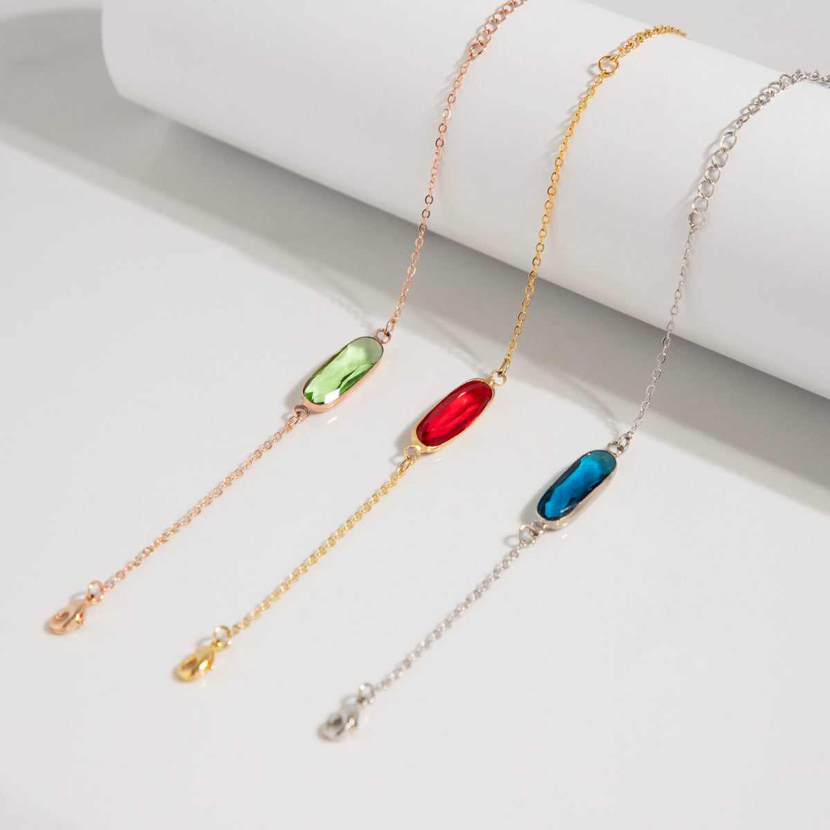 Three bracelets with green, red, and blue rectangular stones arranged on a white surface
