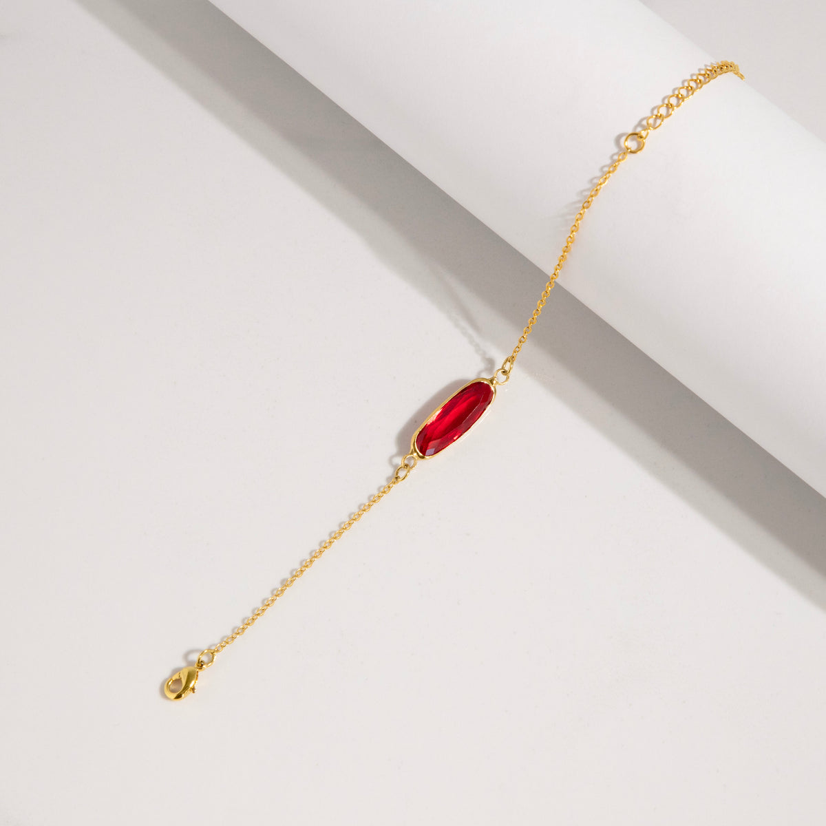Bracelet with red rectangular stone and gold-tone adjustable chain laid diagonally on a white surface