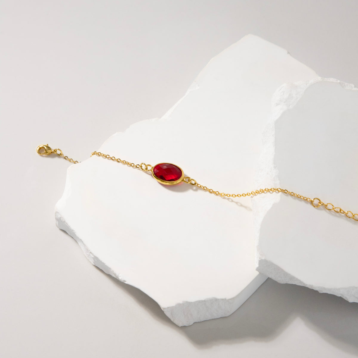 Gold-tone bracelet with red faceted oval stone and adjustable chain on a white sculptural surface