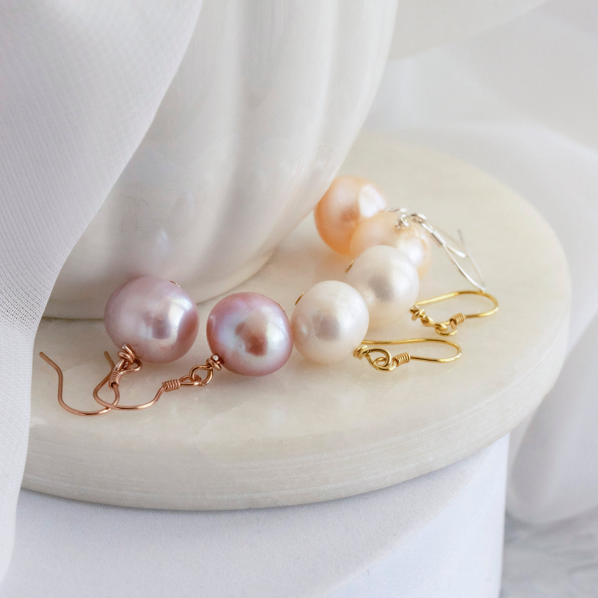 Assorted dangle earrings with round white, peach, and pink-toned drops displayed on a pale surface