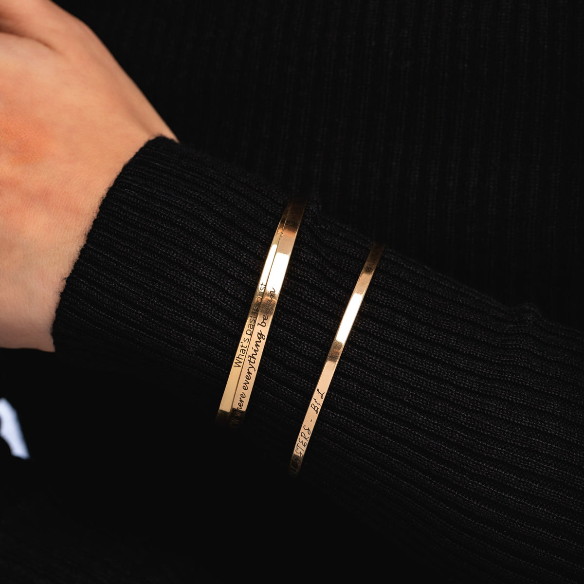 Three gold-tone engraved cuff bracelets worn over a black knit sleeve