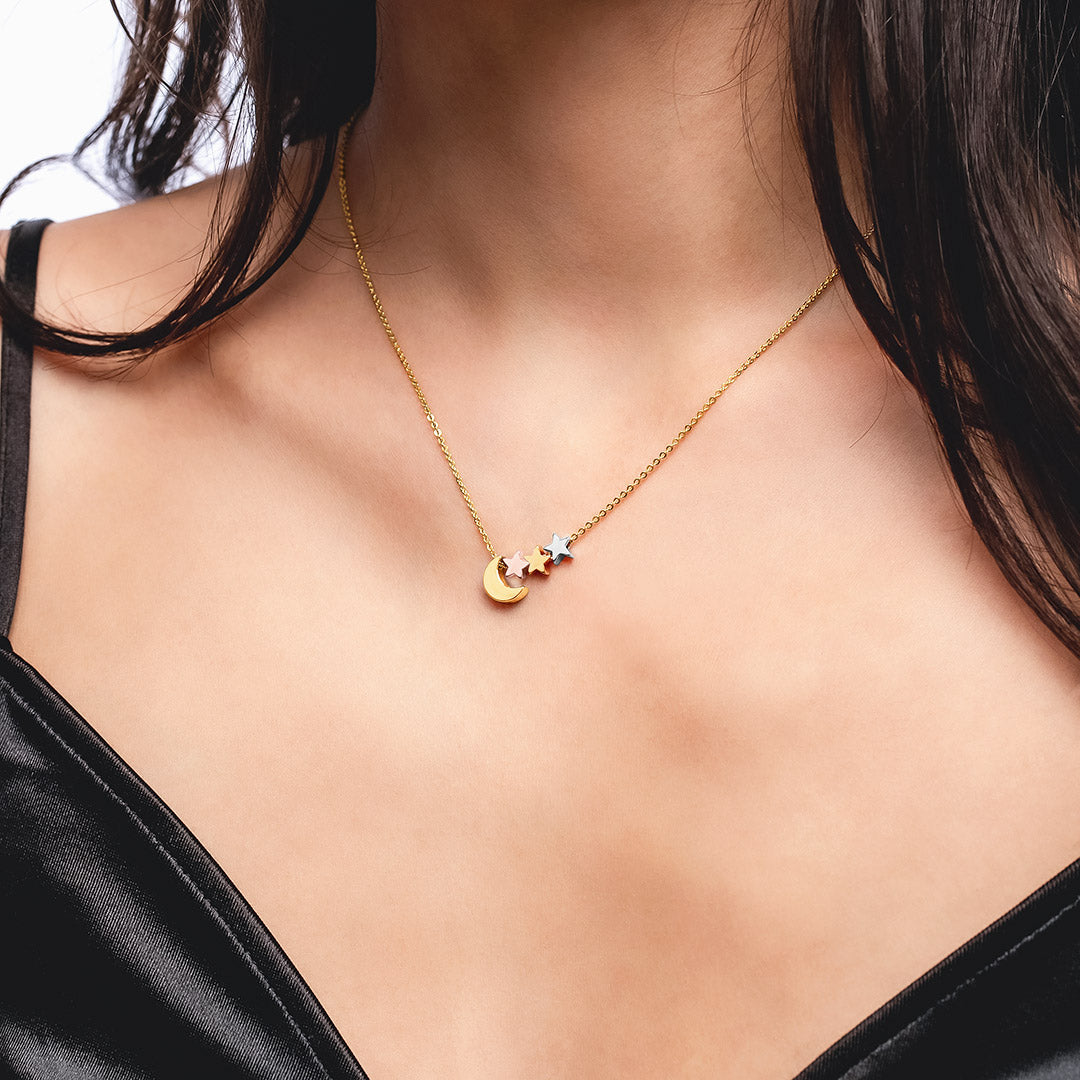 Gold-tone necklace with a crescent moon and three star charms, worn on the neck against a black top