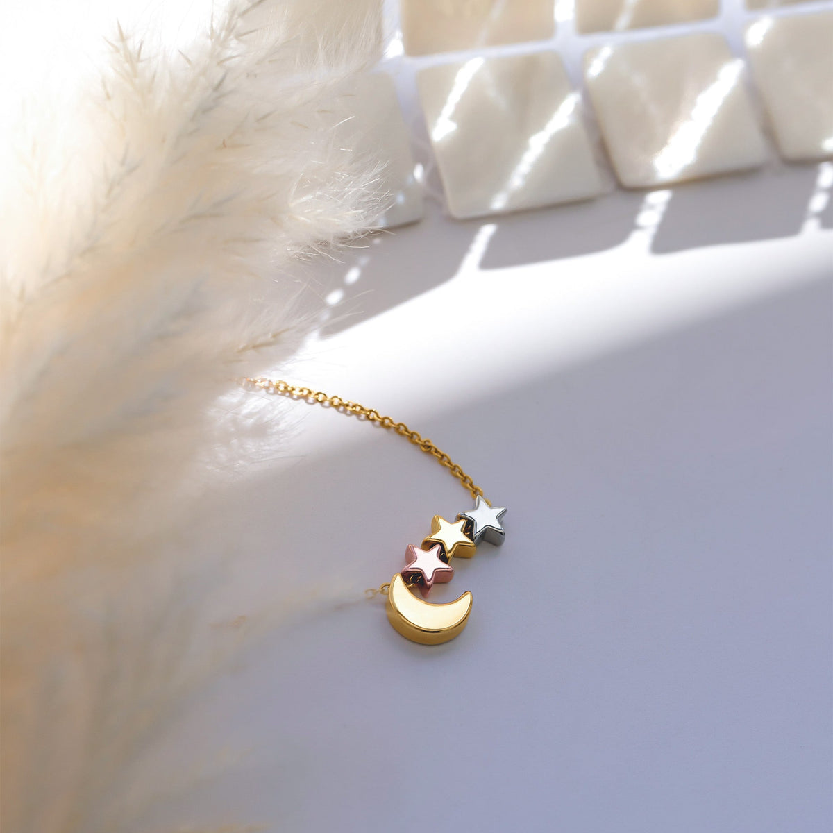 Gold-tone necklace with a crescent moon and three star charms in mixed tones, arranged on a white surface