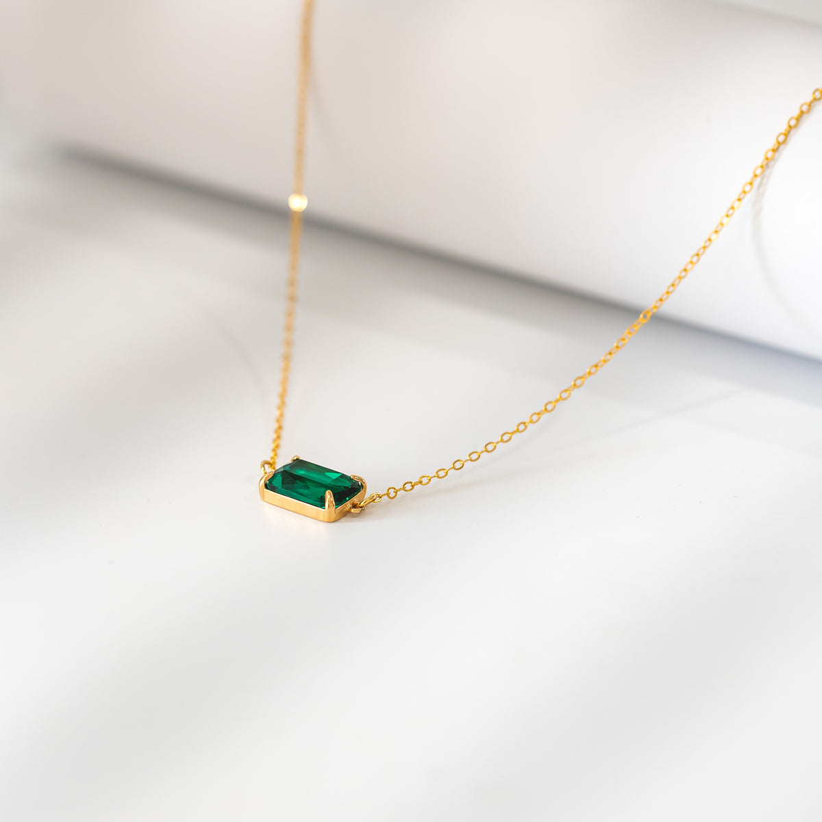 Gold-tone necklace with a rectangular green faceted pendant displayed on a white surface