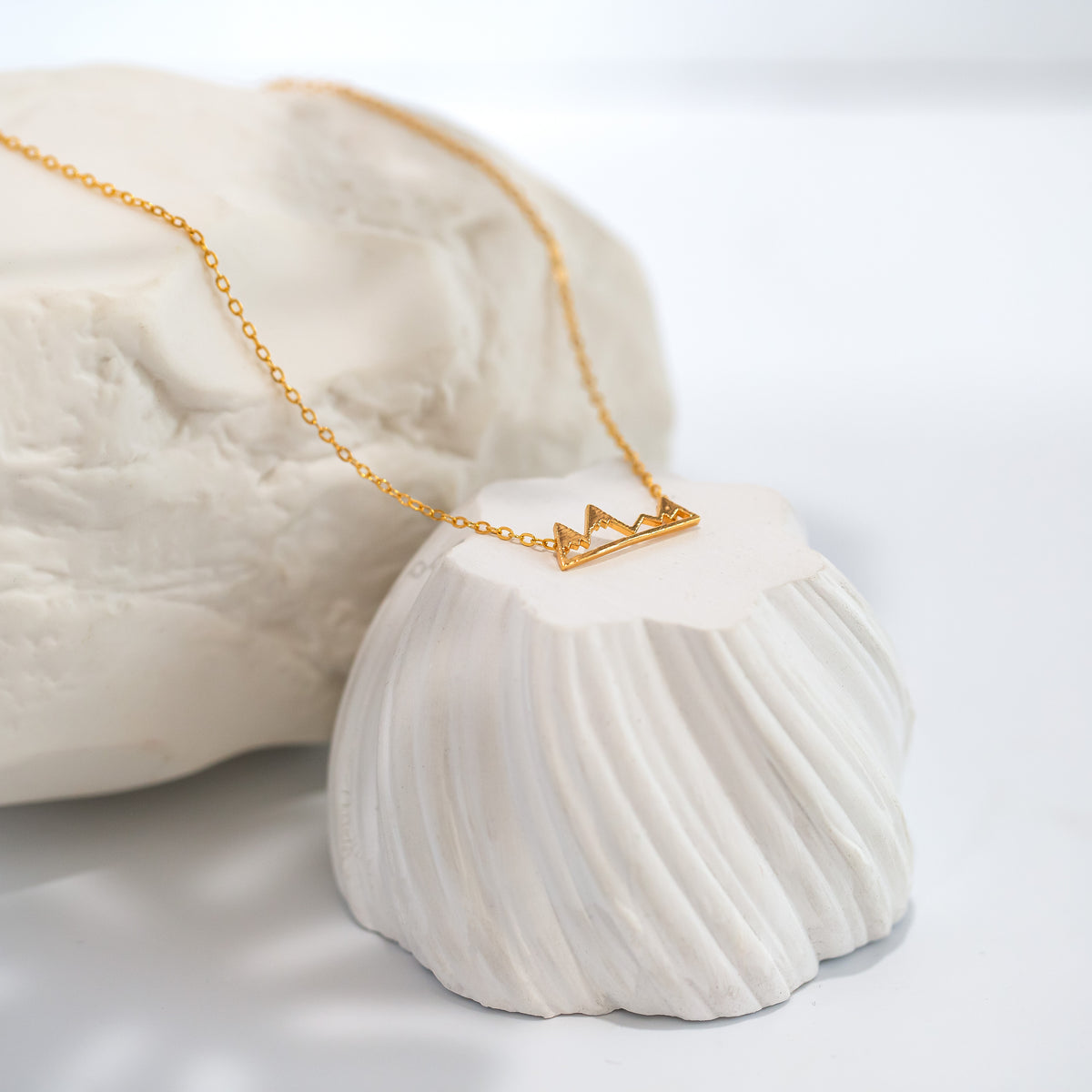 Gold-tone necklace with an open mountain-shaped pendant displayed across white sculptural props